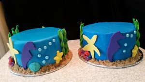 Two cakes with blue icing and sea animals on them.