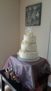 A three layer cake with white frosting and silver ribbon.