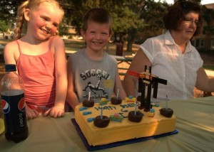 A boy and two girls sitting in front of a cake.