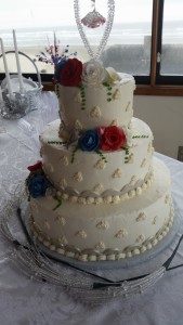 A three layer cake with red and blue roses on top.