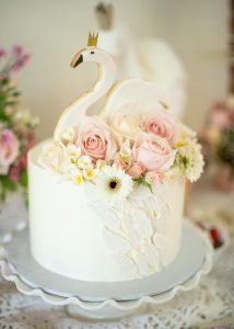 A white cake with flowers and swans on top.